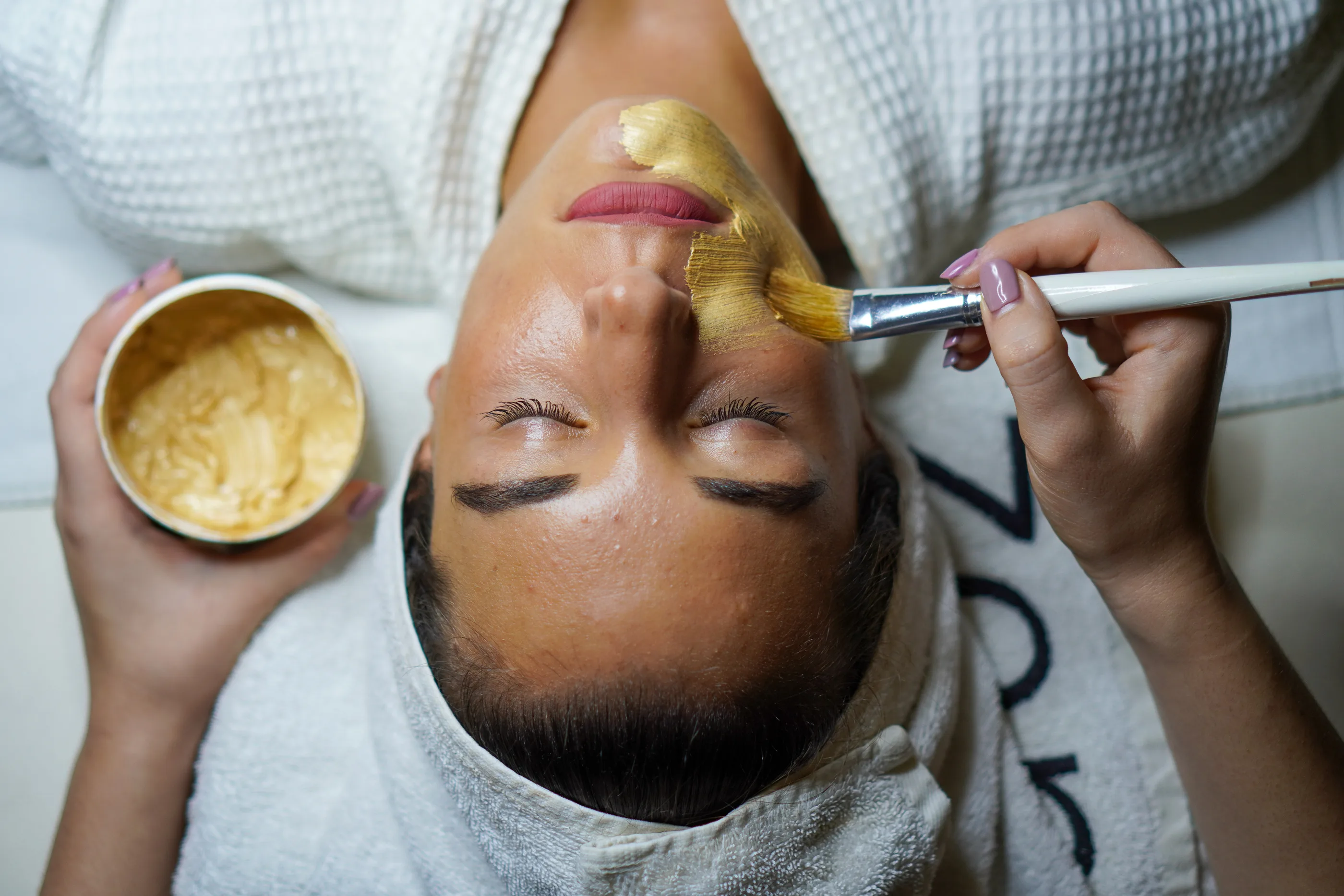 Organic gold mask being applied with brush during a natural radiance facial at Safe Haven Spa